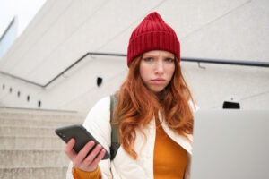 Woman checking details on a laptop and smartphone, appearing cautious while verifying information online